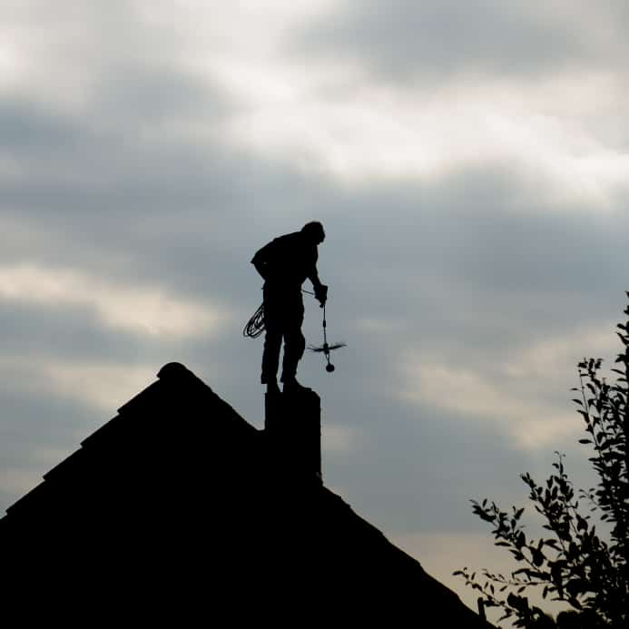 Chimney Sweep standing on top of the chimney on the roof of a home | Estates Chimney And Fireplace LLC | Holland, PA 267-685-0530